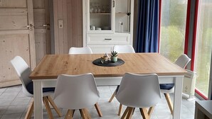 Un coin repas avec une table en bois, des chaises blanches, un buffet contenant de la verrerie et une fenêtre avec des rideaux.
