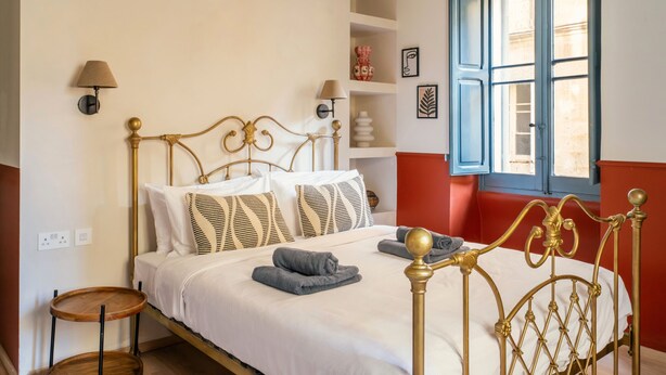 Ein Bett mit goldfarbenem Gestell, weißer Bettwäsche und einer roten Akzentwand.