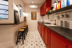 Eine Küche mit roten Schränken, einer schwarzen Arbeitsplatte, einer weißen Spüle und einem gefliesten Boden. Es gibt Hocker an der Bar und eine Tafel an der Wand.