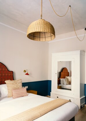 A bedroom with a bed, a white wardrobe, a mirror, a hanging light fixture, and a wall-mounted lamp.