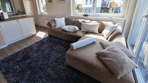 A modern living room with a sofa, a rug, and a view of the outside. - Haus am Merr auf Fehmarn OT Westerbergen (Fehmarn)