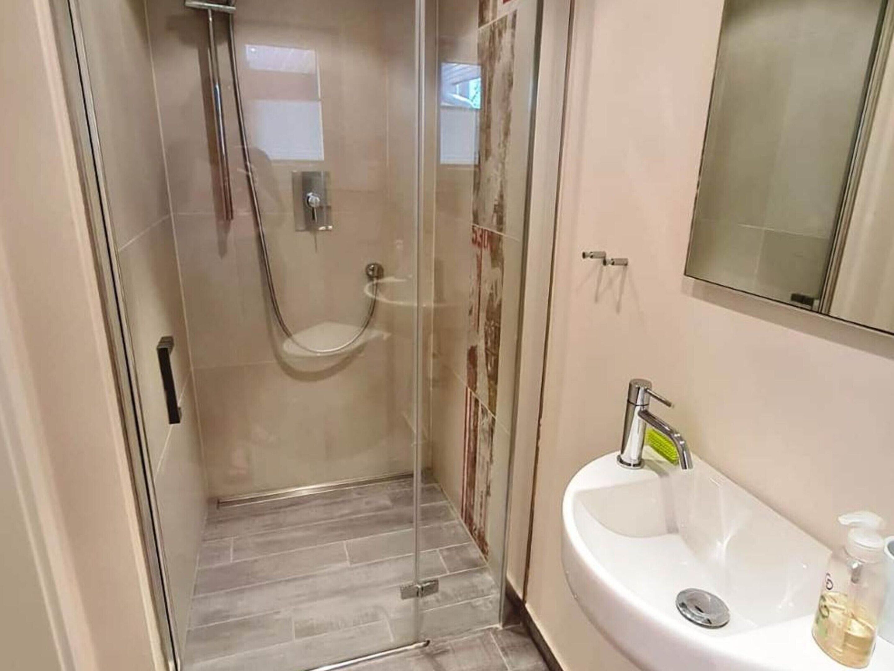 A modern bathroom with a glass-enclosed shower, a white sink with a soap dispenser, and a mirror above the sink.