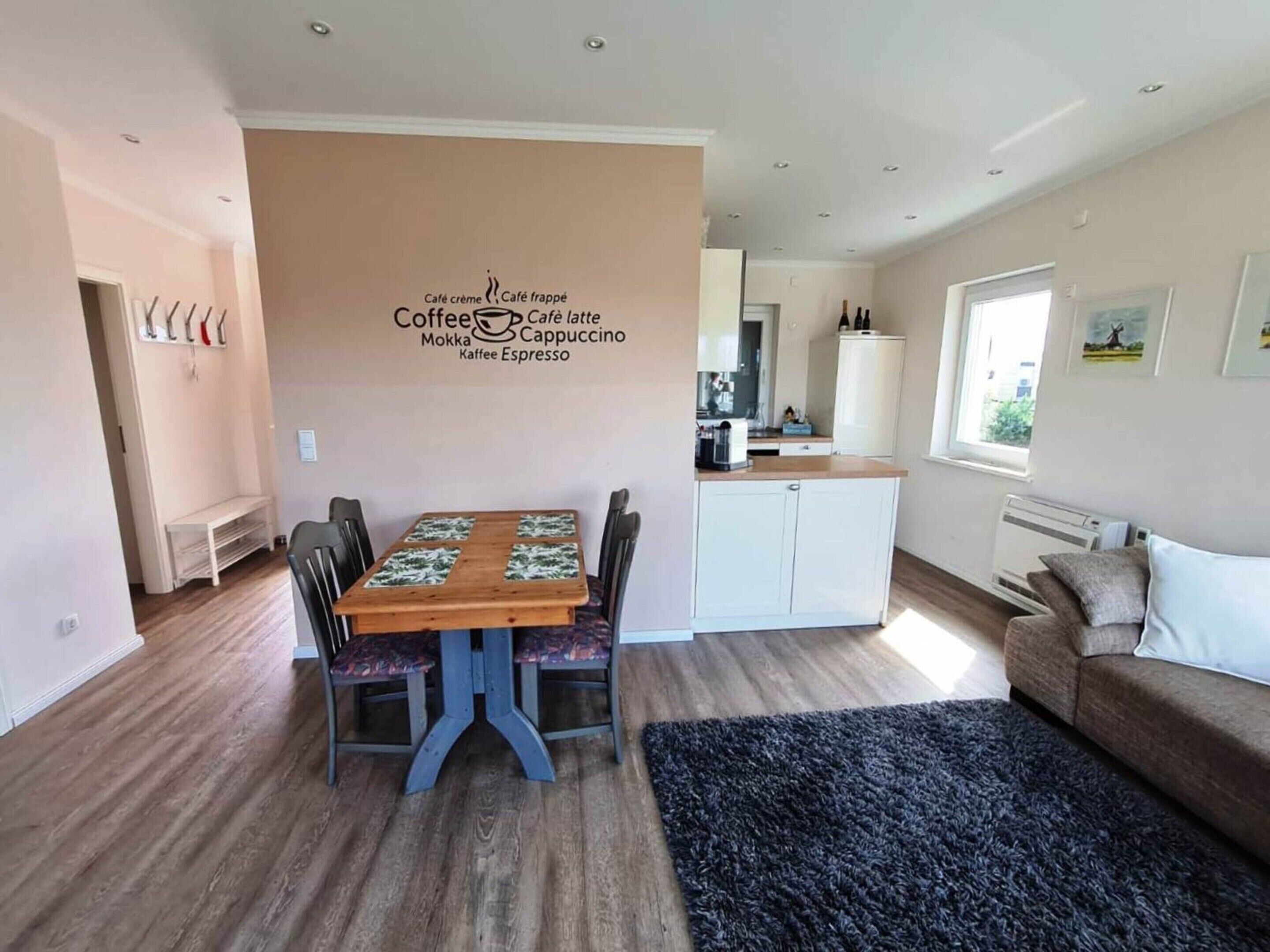 A cozy living room with a dining area, a kitchenette, and a wall-mounted sign listing coffee and tea options.