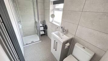 A compact bathroom with a glass shower enclosure, a sink, and a toilet.