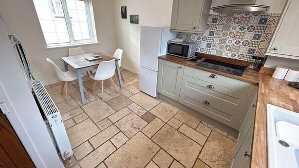A compact kitchen with a dining area, featuring a tiled backsplash, a microwave, and a small refrigerator.