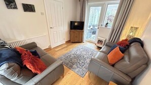 A living room with two grey sofas, a wooden coffee table, a patterned rug, a television, and a door leading to a balcony.