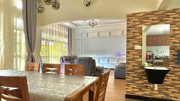 Un comedor con mesa y sillas de madera, una cocina con salpicadero de piedra y un salón con sofá y cortinas.