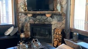 Un salón acogedor con chimenea de piedra, un televisor montado y un sofá de cuero cómodo.
