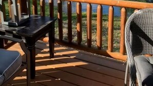 Una terraza de madera con baranda que da a un lago, rodeada de árboles.