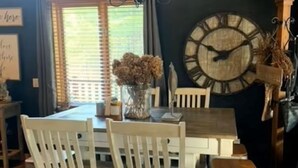 Un comedor con una mesa y sillas de madera, un reloj de pared grande y un letrero que dice "The Farmhouse".