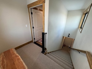 A staircase with a wooden handrail and carpeted steps leading to a door.