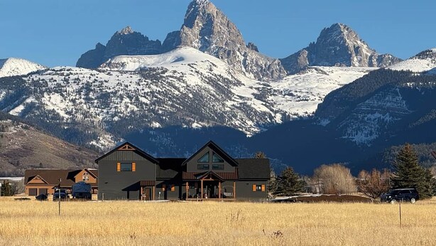 Un chalet doté d’une vue imprenable sur les montagnes, avec un bâtiment principal comprenant une grande véranda et de nombreuses fenêtres.