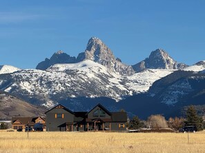 A lodge with a prominent mountain backdrop, featuring a main building with a large porch and multiple windows. - 1BR Teton View Getaway w/ Hot Tub near Skiing & Nat’l Parks (Driggs)