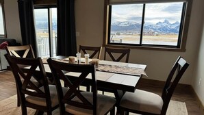 Un coin repas avec une table et des chaises, une vue sur les montagnes par la fenêtre et une porte donnant sur un balcon.