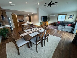 A modern kitchen with wooden cabinets, a dining table with chairs, a flat-screen TV, and a ceiling fan. - 1BR Teton View Getaway w/ Hot Tub near Skiing & Nat’l Parks (Driggs)