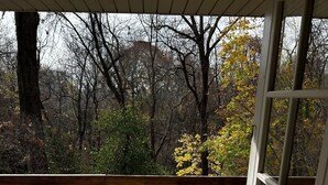 Una terraza de madera con barandilla, con vista a un área boscosa con follaje otoñal.