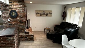 Una sala de estar moderna con chimenea de ladrillo, un comedor con mesa y sillas blancas, un sofá de cuero negro y una guitarra en la pared.