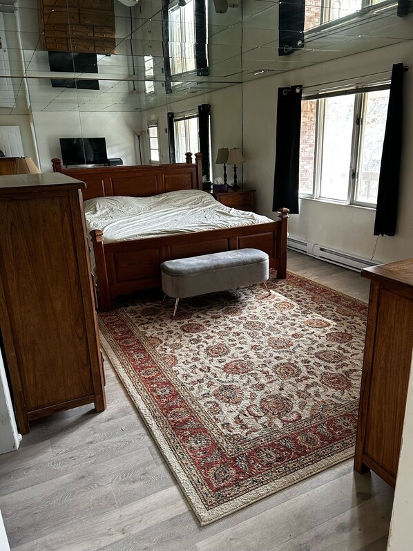 Un dormitorio con una cama de madera, un banco, una alfombra grande y un espejo en la pared.