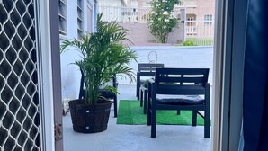 Una puerta que da a un patio exterior con un felpudo, un banco y plantas en macetas.