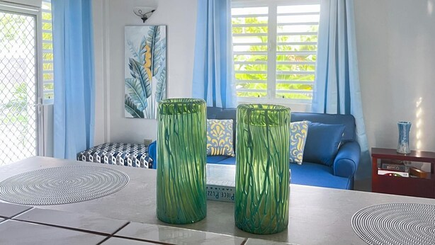 Una sala moderna con un sofá, dos jarrones verdes, un ventilador de techo y una ventana con cortinas azules.
