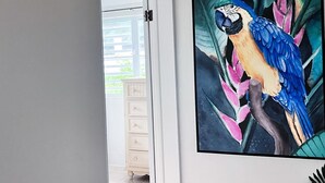 Una habitación con un aparador blanco, un cuadro enmarcado de un guacamayo colorido y una puerta que da a un espacio exterior.