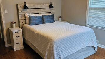 Een slaapkamer met een bed, nachtkastje, dressoir, plafondventilator en raam met jaloezieën.
