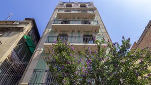 Un edificio de varios pisos con balcones y un árbol con flores moradas al frente.