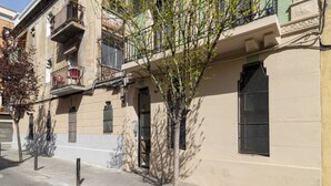 Un edificio con fachada color beige, balcones con barandillas de metal y un árbol en la parte delantera.