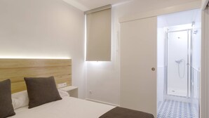 Habitación de hotel con cama, mesita de noche y zona de ducha.