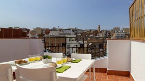 A rooftop terrace with a table set for breakfast, including croissants, orange juice, and a small plant. - OLA LIVING CALID ATTIC (Hospitalet de Llobregat)