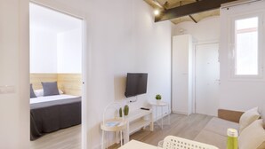 A modern, well-lit room with a bed, a TV, a small table with a plant, and a sofa. - OLA LIVING CALID ATTIC (Hospitalet de Llobregat)