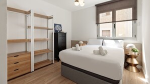 Een moderne slaapkamer met een bed, nachtkastjes, een kledingkast en een raam met jaloezieën.