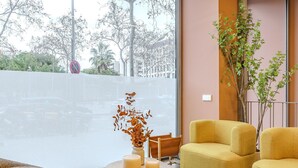 A modern interior with a large window, a wooden table with candles, a yellow armchair, and a potted plant.