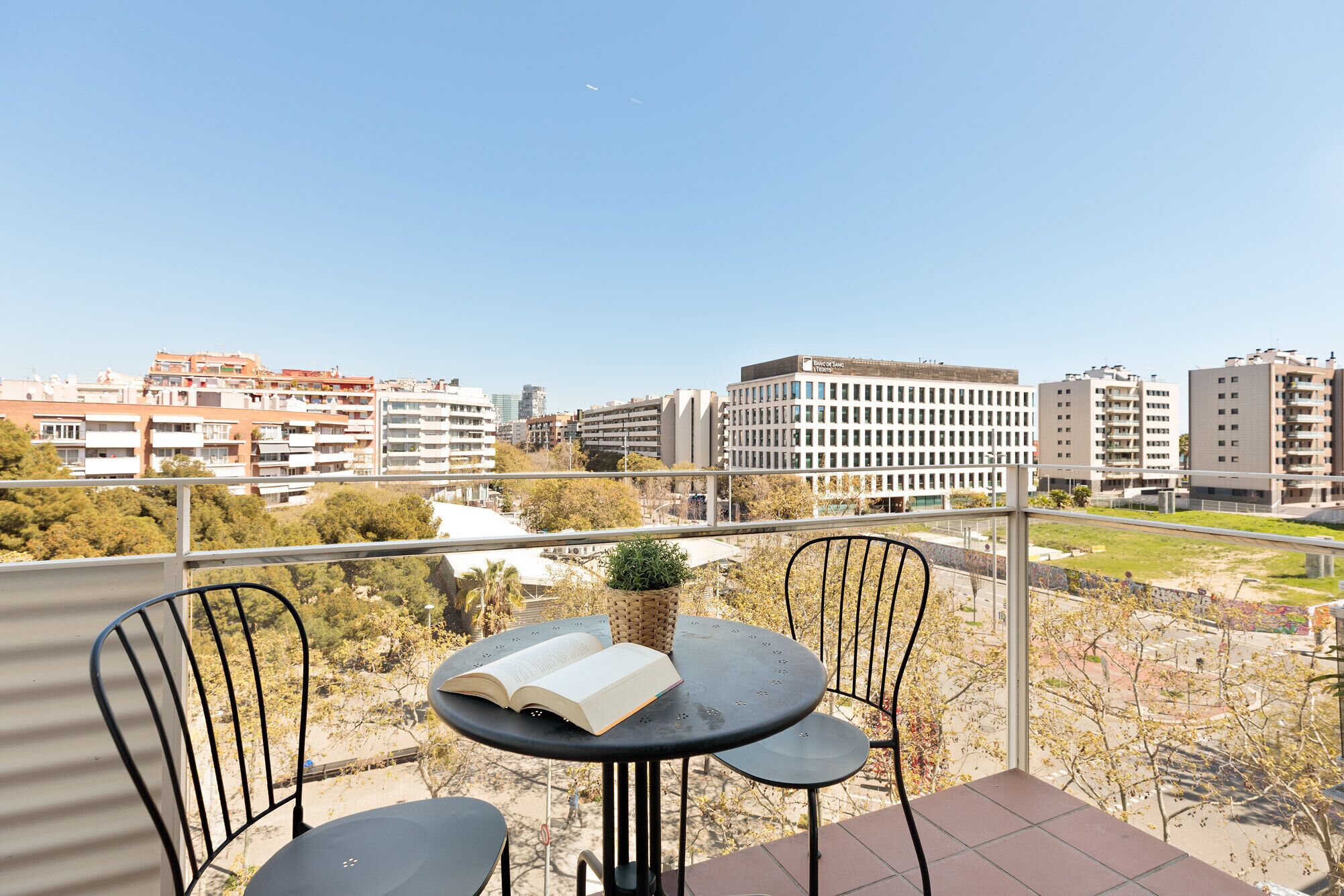 Un balcón con una mesa y sillas, con vistas a un paisaje urbano con diversos edificios.