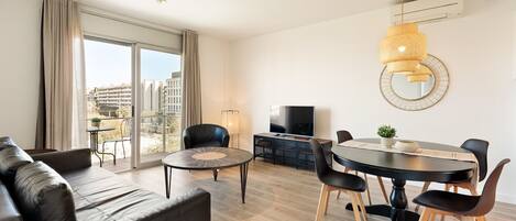 Een moderne woonkamer met een bank, een eettafel met stoelen, een televisie en een groot raam met gordijnen.
