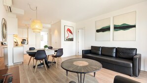 Ein modernes Wohnzimmer mit einer schwarzen Ledersofa, einem runden Couchtisch und einem Essbereich mit weißem Tisch und Stühlen.
