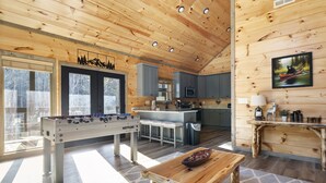 A cozy wooden cabin interior with a foosball table, kitchen area, and large windows. - Private Pool! Newly built! Convenient location! (Sevierville)