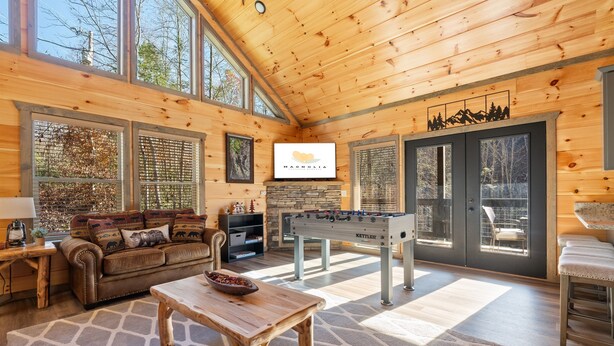 A cozy wooden interior with a sofa, table, foosball table, and large windows. - Private Pool! Newly built! Convenient location! (Sevierville)
