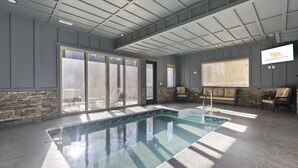An indoor swimming pool with a stone wall and glass doors leading to a patio area. - Private Pool! Newly built! Convenient location! (Sevierville)