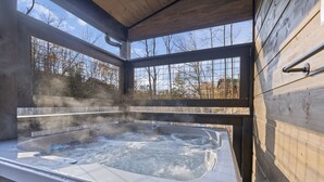 A hot tub with steam rising, surrounded by wooden walls and large windows. - Private Pool! Newly built! Convenient location! (Sevierville)