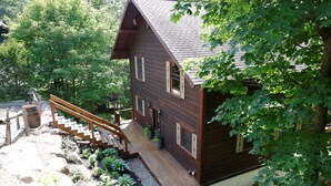 Een houten chalet met een houten terras, een trap en een tuin met planten en een vat.