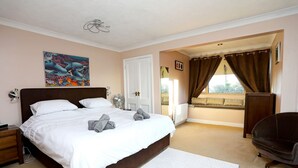 A bedroom with a large bed, a bedside table, a chair, a window with curtains, and a painting on the wall. - Picturesque Family Hideaway Chipping Ongar Essex (Ongar)