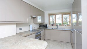 A modern kitchen with a large island, stainless steel appliances, and a window providing natural light. - Picturesque Family Hideaway Chipping Ongar Essex (Ongar)