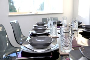 A dining table set with plates, bowls, and clear glasses, with chairs on either side. - Picturesque Family Hideaway Chipping Ongar Essex (Ongar)