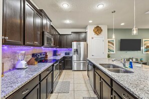 Una cocina moderna con armarios oscuros, electrodomésticos de acero inoxidable, encimeras de granito e iluminación debajo de los gabinetes.