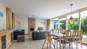 A spacious living area with a dining table, chairs, a sofa, and a fireplace. - Bungalow in North Holland Near the Beach (Sint Maartensvlotbrug)