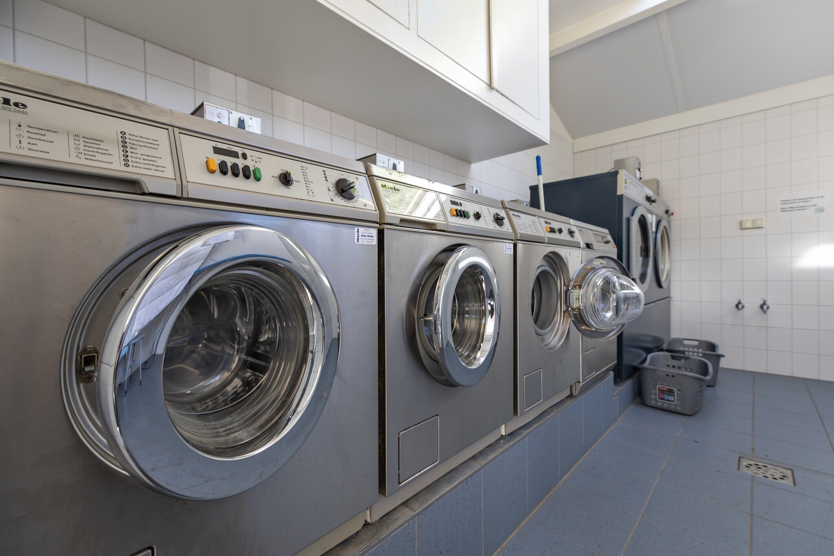 A row of stainless steel front-loading washing machines in a commercial laundry facility.