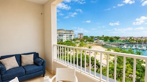 Ein Balkon mit einem blauen Sofa und einem weißen Stuhl, der auf einen Yachthafen mit Booten und einen Strand blickt.