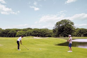 Ein Golfplatz mit zwei Spielern, einem Teich und Bäumen im Hintergrund.