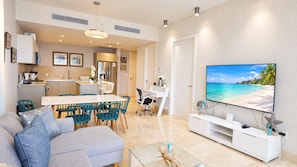 A modern living room with a flat-screen TV, a sofa, a dining area, and a kitchen.